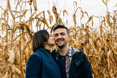 Woman kissing happy smiling man on the cheek standing in autumn in a cornfieldの写真素材