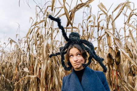 A woman with a distorted face and a toy of a furry large spider on her head. Concept of decorations for the celebration of Halloween.の写真素材