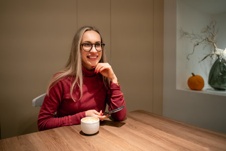 young woman enjoying coffee and using smartphone in cozy cafe.の写真素材