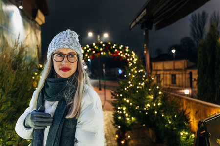 happy young woman in cozy winter attire admiring holiday lights.の写真素材