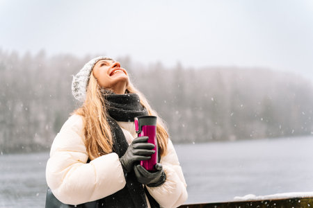 smiling woman enjoying snowfall with a thermos in winter natureの写真素材