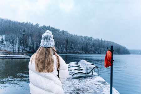 Woman standing on a snowy lakeside, looking at the view wearing winter clothesの写真素材