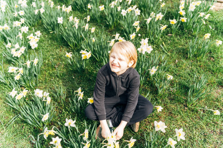 Happy boy sitting in a field of blooming daffodils, enjoying springtime natureの写真素材