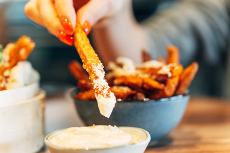 Close-up of crispy sweet potato fries being dipped into rich creamy sauceの写真素材