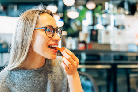Smiling woman with glasses enjoying a crispy snack in a modern cafeの写真素材