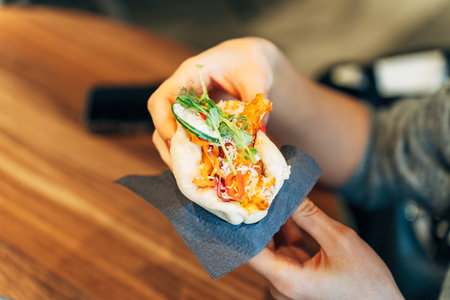 Woman Holding a Bao Bun with Fresh Ingredients in a Casual Restaurant Settingの写真素材
