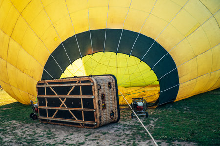 Partially inflated yellow hot air balloon and passenger basket on grass, close-up viewの写真素材