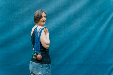 Smiling Woman with Reusable Bag Posing Against a Blue Backgroundの写真素材