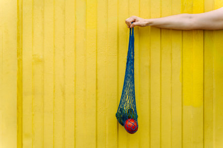 Eco-friendly mesh tote with fresh veggies isolated on yellow background