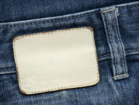 Blank leather jeans label sewed on a blue jeans. Can be used as background for your text.
