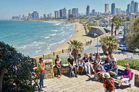TEL AVIV, ISRAEL - APR 11, 2014: A group of turists near the Mediterranean  beach and Tel Aviv, Israel boradwalk with the city sky line and towers in the backgroundのeditorial素材