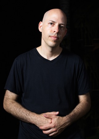 Low-key portrait of a 40 year old bald man on black background with crossed handsの写真素材