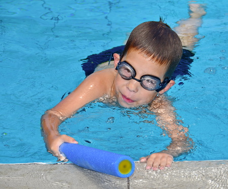 A 6-year-old boy having fun in the swimming pool with a toy water squirt gunの写真素材