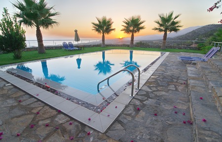 Palm trees, lounge chairs, and pool on a summer vacation - Sunrise and mist over the Cretan mountains with picture-perfect palm trees reflecting in a pool in Malia, Crete near Heraklionのeditorial素材