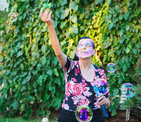 A modern grandmother playing with soap bubbles from a huge bubble blowerの写真素材