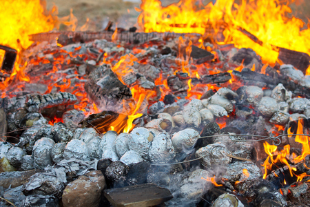 Baked potatoes covered with aluminum foil roasting in a Lag Baomer bonfire with orange flames and firewood in a secular suburb of Tel Aviv, Israelの写真素材