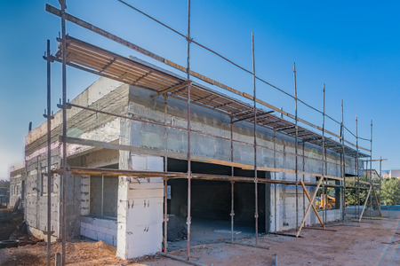 A Mediterranean,  brick and concrete house under construction, covered with scaffolding