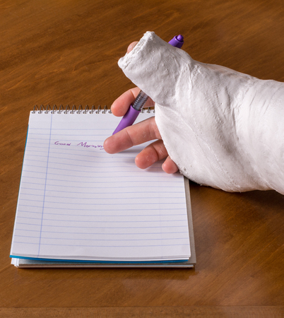Person wearing an arm cast after breaking his wrist trying to write a note on a piece of paperの写真素材