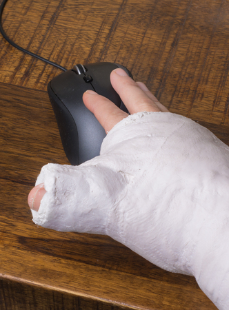 A person wearing an arm cast after breaking their wrist having difficulty using a computer mouseの写真素材