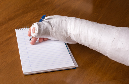 Person wearing an arm cast after breaking their wrist trying to write a note on a piece of paperの写真素材