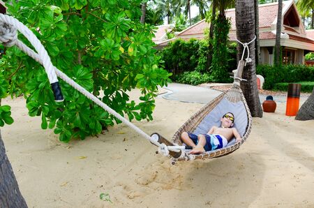 A 10 year old boy enjoying a hammock on the beautiful tropical island beach of Koh Samui, Thailandの写真素材