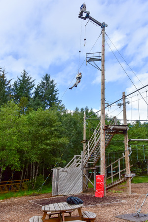 Young teenage woman challenging herself high up in a treetop rope park adventure in Ben Nevis, Scotlandの写真素材