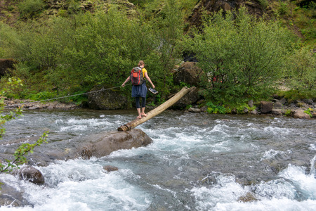 GLYMUR, ICELAND - JULY 19, 2018: A woman crossing the dangerous and slippery river near the Beautiful Glymur waterfall on the edge of Hvalfjordur fjord, Icelandのeditorial素材