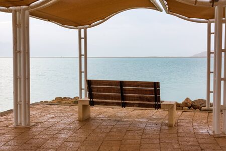 Creative image of the  Dead Sea at dawn blue hour before sunrise, featuring a bench overlooking the seaの写真素材