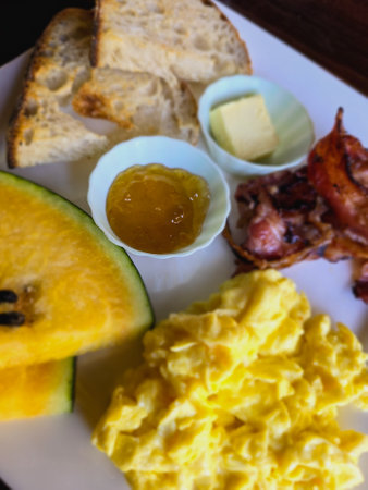 Breakfast with scrambled eggs, bacon, melon and orange jamの写真素材