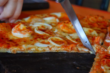 Pizza with seafood on a black plate, close-up.