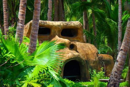 Tropical garden with green palm trees and giant stone house.の写真素材