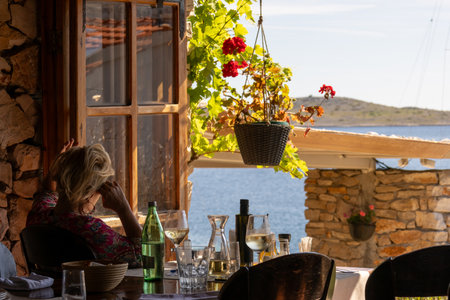 Woman sitting in a restaurant with a view on the sea and mountainsの写真素材