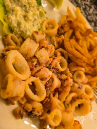 Fried squid rings with french fries and salad on a plate.
