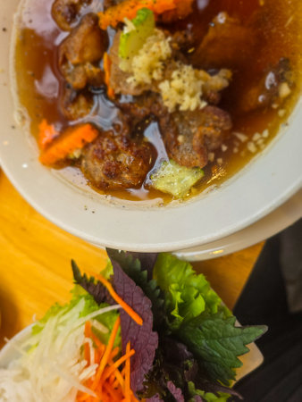 Thai style spicy soup with pork in white bowl on wooden table