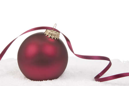 A Red Christmas Bauble with Ribbon on Snow Backgroundの写真素材