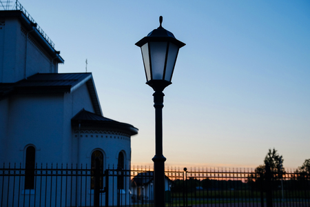 Construction of white brick with a dark roof. Lights are at the sidewalk. Sun at sunset.の写真素材