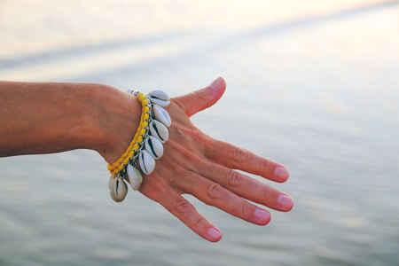 Close-up of the hand of a gentle girl with a bracelet made of seashells. On the background of water.の写真素材