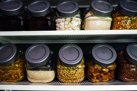 Various raw cereals, grains, beans and pasta for healthy cooking in glass jars on kitchen shelf,...