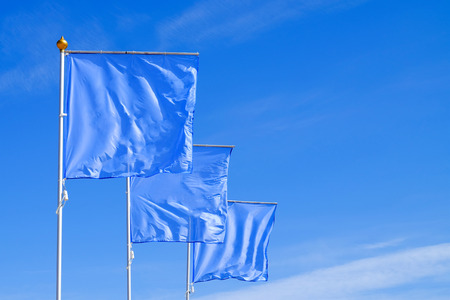 Blue flags waving in the wind against the cloudless sky. Perfect layout to add any logo, symbol or sign.の写真素材