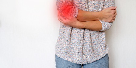 Pain area red background. The girl grabbed his hand in pain. Suffers from diseases of the joints. The concept of health.の写真素材
