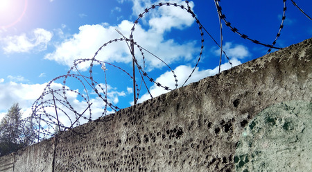Barbed wire on a dark fence. Against a blue sky with cloudsの写真素材