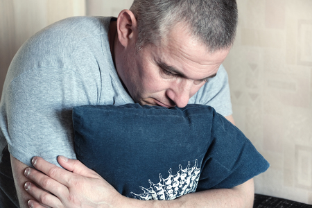 Sadness, absolute loneliness. Top view of depression unhappy sad man sitting hugging pillow feeling unnecessaryの写真素材