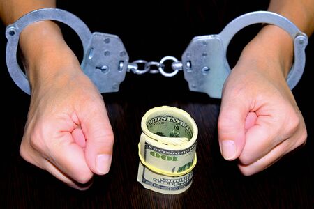 Handcuffed hands clenched into a fist. A wad of dollars tied with a rubber band