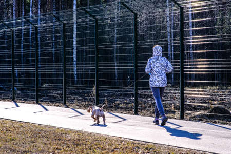 A girl on a run on an asphalt path. A dog is running on a leash next to me. The Park is fenced....