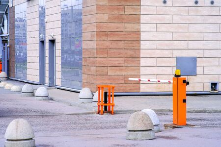 Concrete road barriers and a pneumatic barrier in orange color with a white stripe and red warning stripes, for the entry of cars. Entrance to the courtyard of an elite residential complexの写真素材