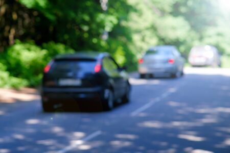 Background, blur, out of focus, bokeh. Soft sunlight through the trees in the forest. Cars are driving on a forest highwayの写真素材