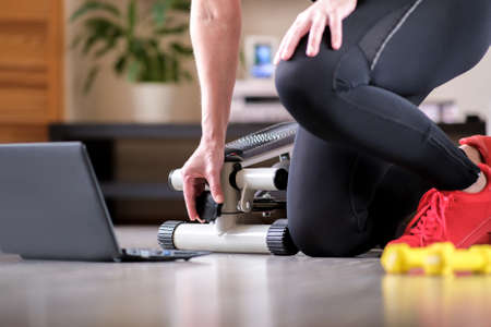The girl turns the handle of the step simulator increases the load. Online fitness training on a step-simulator. Sports at home during the quarantine periodの写真素材