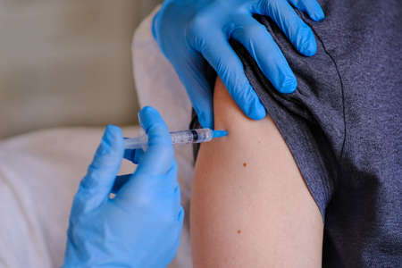 The doctor has a syringe with the vaccine in his hand, an injection in his shoulder. Preventing the spread of the epidemicの写真素材