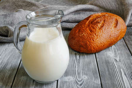 Simple food on the table, milk in a jug, and freshly baked crusty bread. Rustic table made of planks. Canvas fabricの写真素材