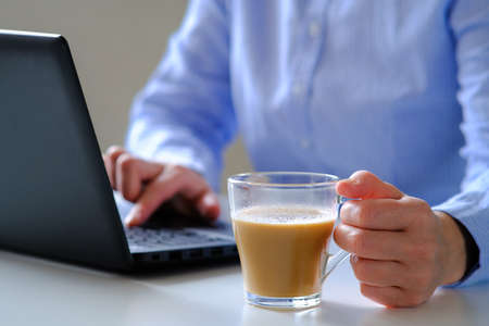 The girl finishes working at the computer for a time out over a Cup of coffee.